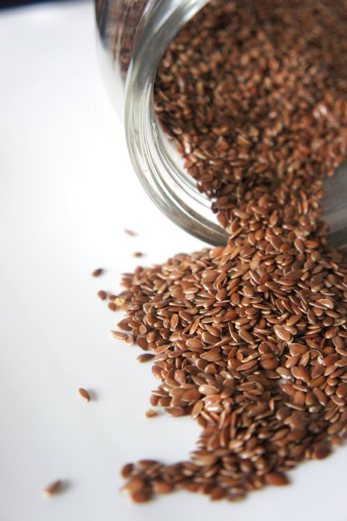 High angle view of flaxseeds spilling from a jar onto a white surface. Perfect for health and food concepts.